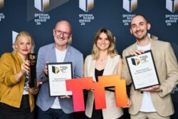 Four people are posing in front of a “German Brand Award 2026” photo backdrop, holding a gold trophy, two certificates of recognition, and a large orange-and-red Messe Düsseldorf logo.