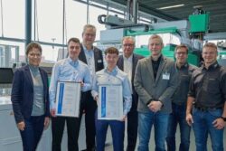 Photo: Frank Kössig and Dennis Sagel holding their certificates for the 2023 Günter Schwank Award, surrounded by other ARBURG employees; Copyright: ARBURG GmbH + Co KG